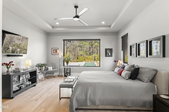 bedroom with a raised ceiling, recessed lighting, baseboards, and light wood finished floors