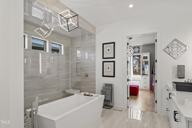 bathroom with recessed lighting, plenty of natural light, marble finish floor, and a freestanding tub