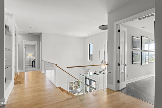 hall with wood finished floors, visible vents, and baseboards