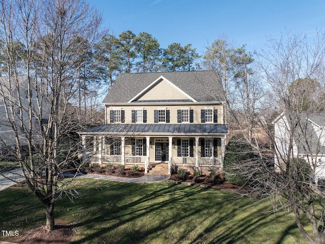 colonial house featuring roof with shingles, a porch, and a front yard