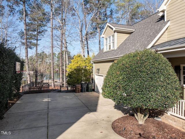 view of side of property featuring a garage, roof with shingles, and fence