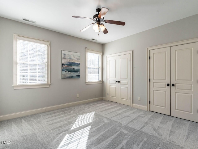 unfurnished bedroom with light carpet, two closets, visible vents, and baseboards