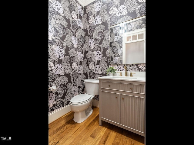 bathroom with wallpapered walls, baseboards, toilet, wood finished floors, and vanity