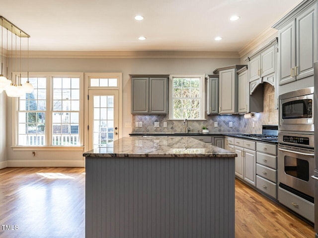 kitchen featuring crown molding, stainless steel appliances, gray cabinets, a kitchen island, and dark stone counters