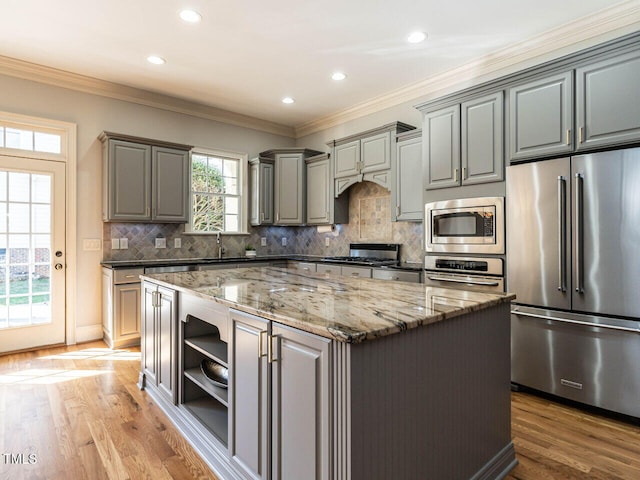 kitchen with gray cabinetry, appliances with stainless steel finishes, ornamental molding, a center island, and dark stone countertops