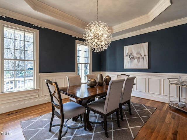 dining area with a tray ceiling, visible vents, a notable chandelier, and wood finished floors