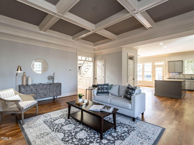 living area with beamed ceiling, coffered ceiling, wood finished floors, and crown molding