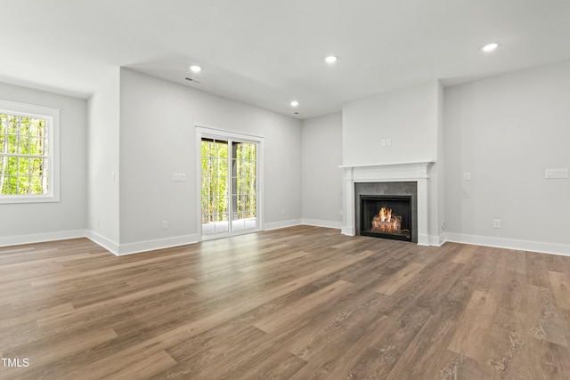unfurnished living room with recessed lighting, plenty of natural light, and a warm lit fireplace