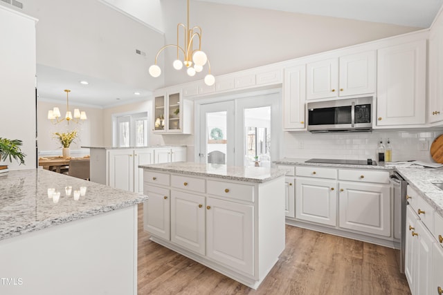 kitchen featuring a center island, pendant lighting, stainless steel microwave, glass insert cabinets, and white cabinets