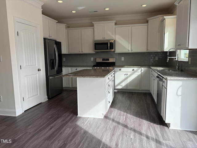 kitchen featuring a center island, stainless steel appliances, white cabinets, a sink, and dark stone countertops