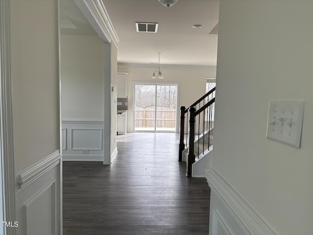 corridor featuring crown molding, dark wood finished floors, visible vents, a decorative wall, and stairs