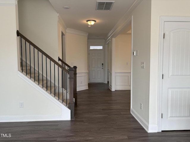 foyer entrance with a decorative wall, dark wood-type flooring, visible vents, stairs, and ornamental molding