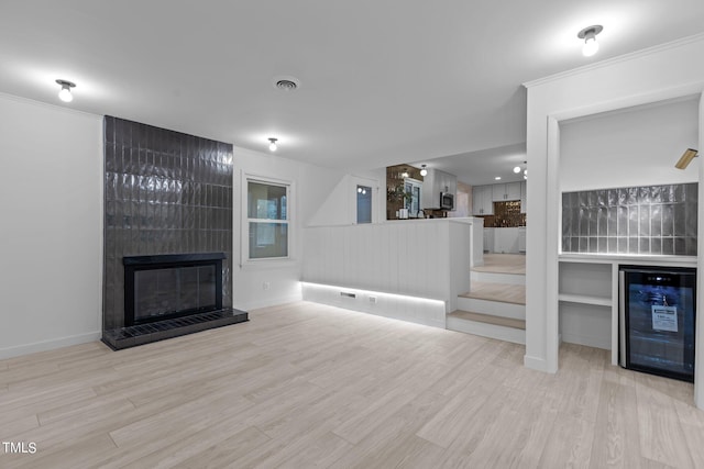 living area with wine cooler, visible vents, light wood-type flooring, a dry bar, and a tiled fireplace