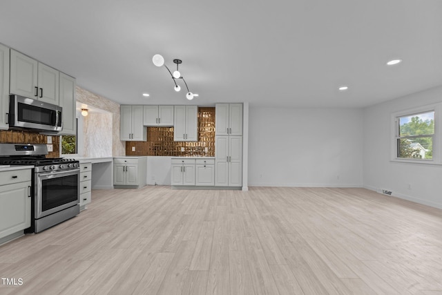 kitchen with light wood finished floors, stainless steel appliances, tasteful backsplash, light countertops, and visible vents