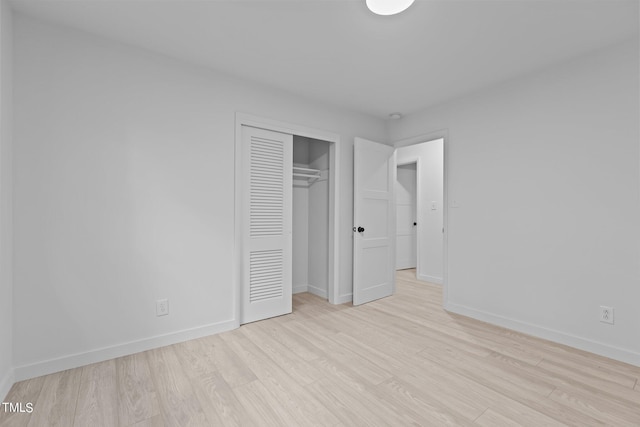 unfurnished bedroom featuring light wood-style flooring, baseboards, and a closet