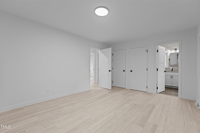 unfurnished bedroom with light wood-style floors, ensuite bath, baseboards, and multiple closets