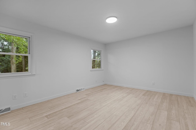 spare room with light wood-type flooring, visible vents, and baseboards