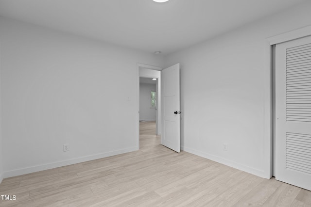 unfurnished bedroom featuring light wood finished floors, baseboards, and a closet