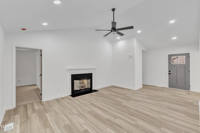 unfurnished living room featuring baseboards, lofted ceiling, a fireplace with flush hearth, light wood-style floors, and recessed lighting