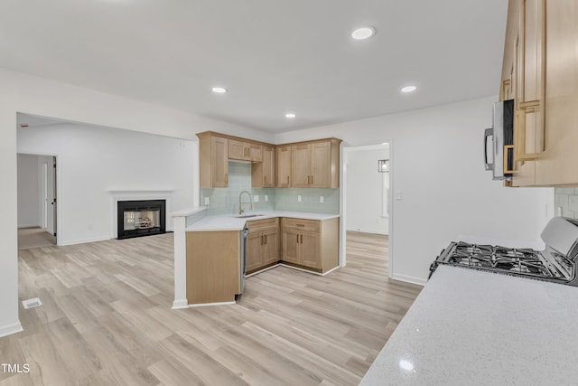 kitchen featuring decorative backsplash, gas range, stainless steel microwave, open floor plan, and a sink