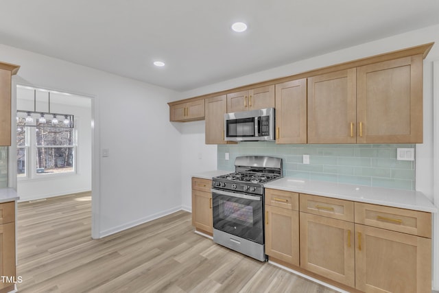 kitchen featuring range with gas cooktop, light wood-style flooring, stainless steel microwave, light countertops, and backsplash