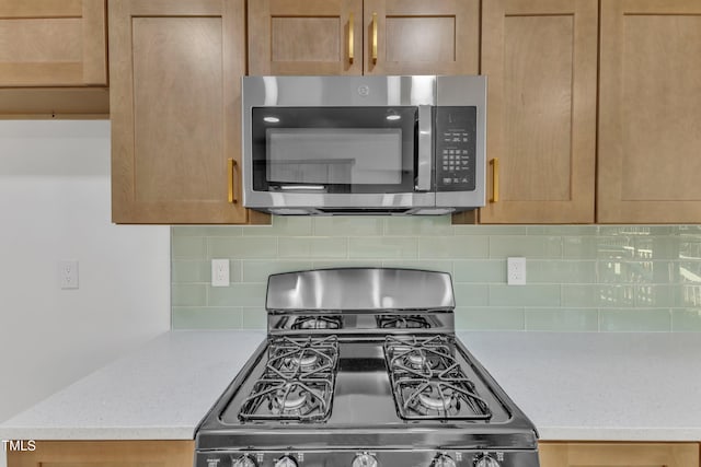 kitchen with gas range, stainless steel microwave, decorative backsplash, and light countertops