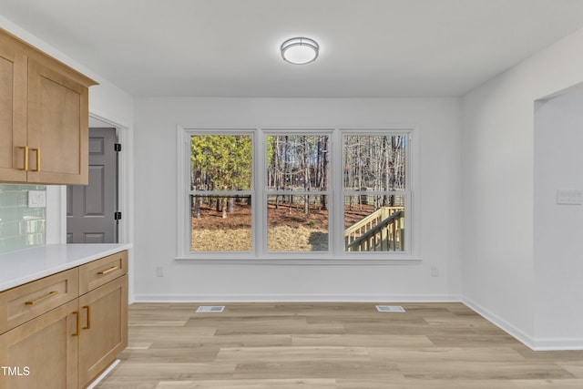 unfurnished dining area with visible vents, light wood-style flooring, and baseboards