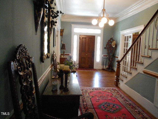 foyer entrance with ornamental molding, stairway, an inviting chandelier, and wood finished floors