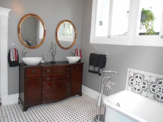 full bathroom featuring double vanity, a soaking tub, baseboards, and a sink