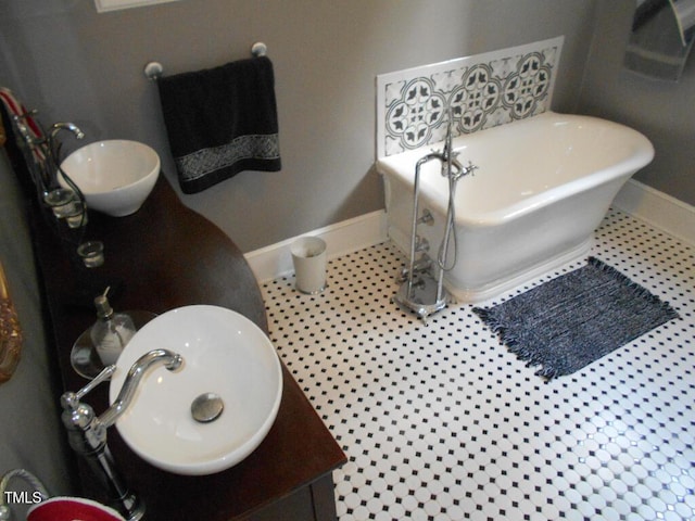 full bath with a freestanding bath, tile patterned flooring, a sink, and baseboards