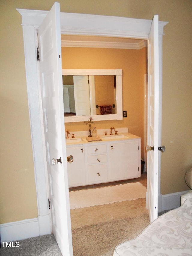 bathroom featuring baseboards, double vanity, a sink, and crown molding