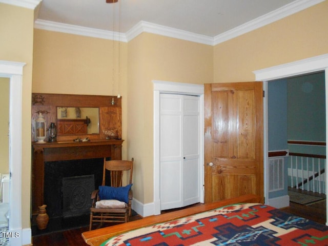 bedroom featuring dark wood-type flooring, a closet, a fireplace, and ornamental molding