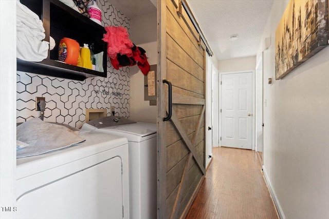 laundry area with a textured ceiling, a barn door, laundry area, wood finished floors, and washer and clothes dryer