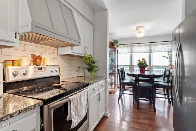 kitchen with stainless steel appliances, light stone countertops, white cabinetry, and custom range hood