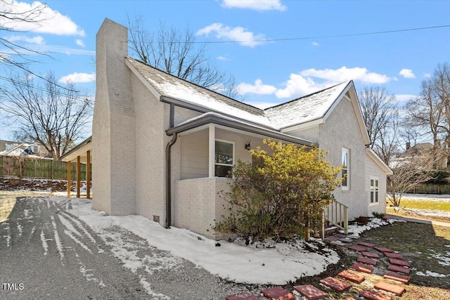 view of snow covered exterior with brick siding, a chimney, and fence