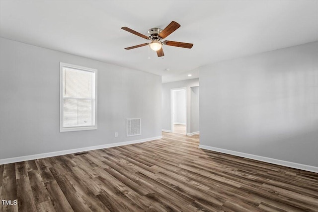 spare room with dark wood-type flooring, visible vents, and baseboards