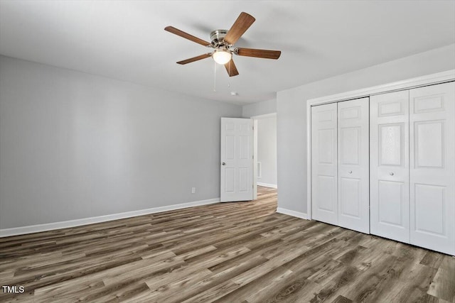 unfurnished bedroom with dark wood-style floors, a closet, baseboards, and a ceiling fan