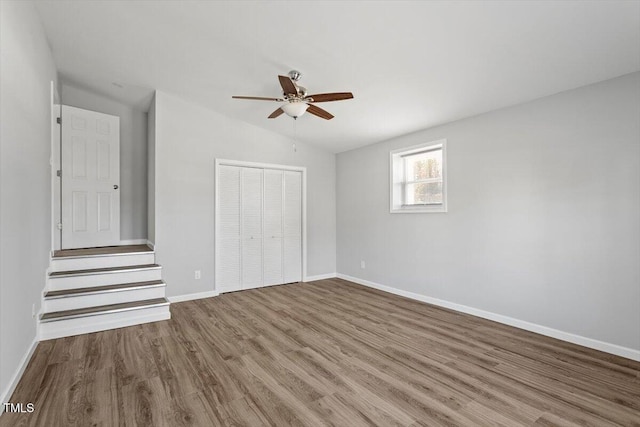 unfurnished bedroom featuring baseboards, a ceiling fan, lofted ceiling, wood finished floors, and a closet