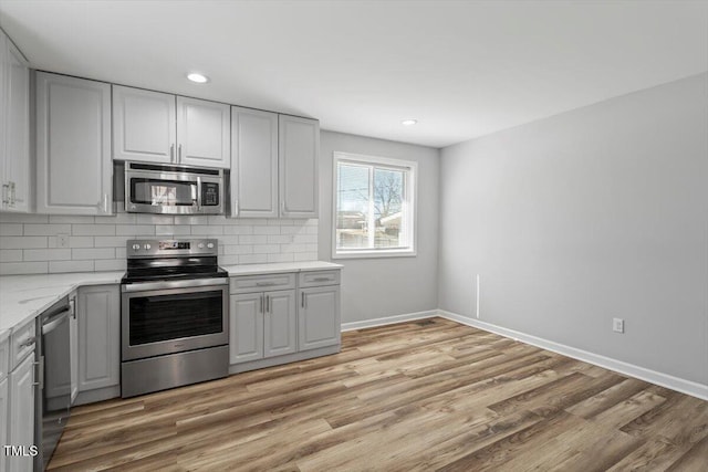 kitchen with stainless steel appliances, light wood-style flooring, baseboards, and tasteful backsplash