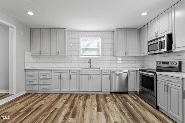 kitchen featuring dark wood-style flooring, stainless steel appliances, light countertops, decorative backsplash, and a sink