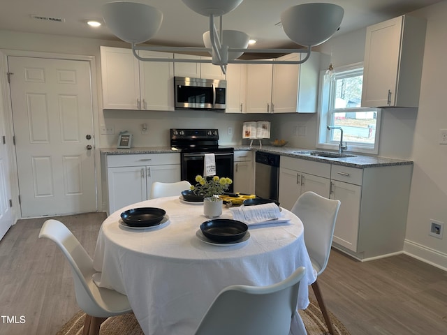 kitchen with stainless steel appliances, wood finished floors, a sink, baseboards, and white cabinets