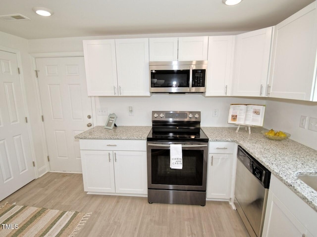 kitchen with recessed lighting, stainless steel appliances, white cabinets, light stone countertops, and light wood finished floors
