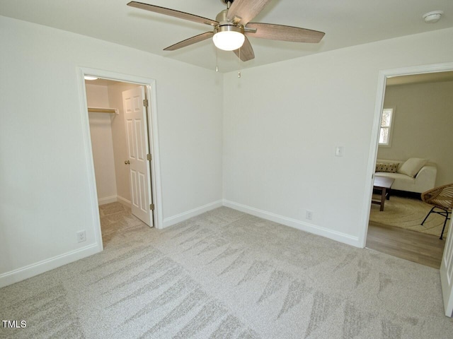 unfurnished bedroom with a ceiling fan, baseboards, a walk in closet, and carpet flooring