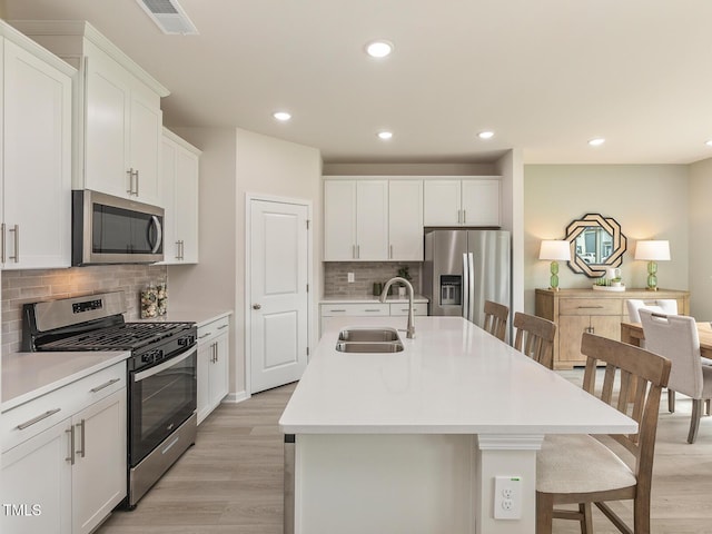 kitchen featuring stainless steel appliances, light countertops, a kitchen island with sink, a sink, and white cabinetry