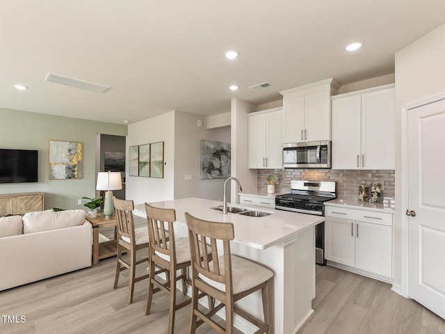 kitchen with stainless steel appliances, visible vents, open floor plan, white cabinetry, and a sink