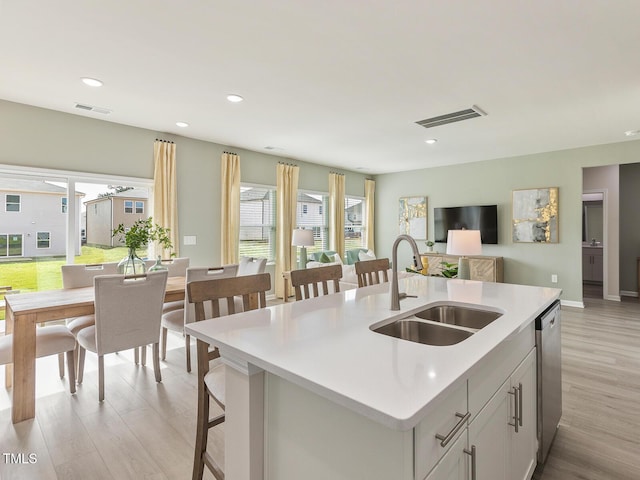 kitchen with a kitchen island with sink, light countertops, a sink, and visible vents