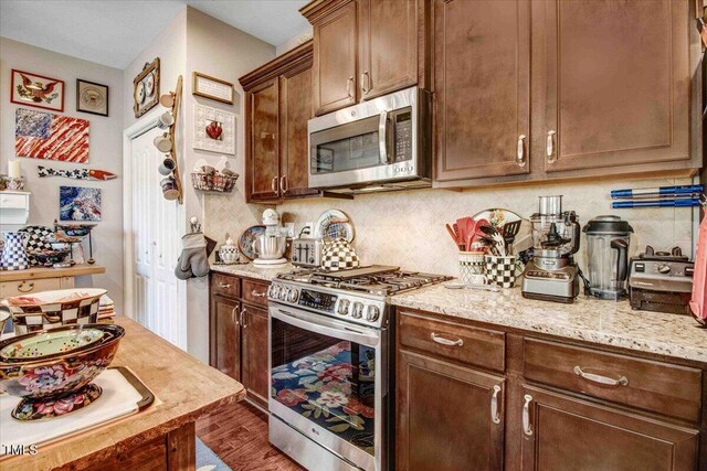 kitchen with wood finished floors, stainless steel appliances, light stone counters, and backsplash