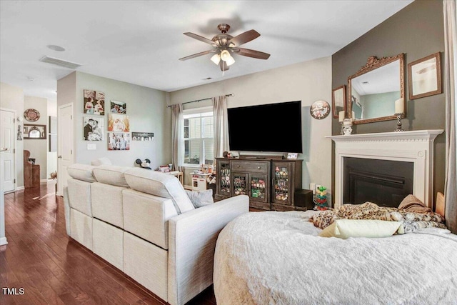 living area featuring dark wood-style floors, visible vents, a ceiling fan, and a glass covered fireplace