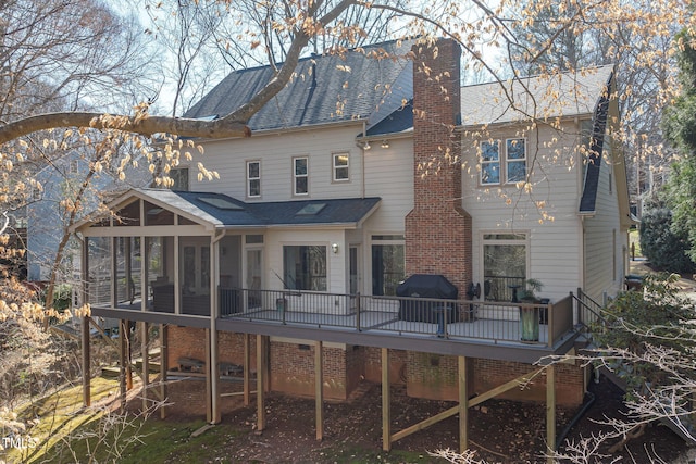 back of house featuring a sunroom, a chimney, a deck, and roof with shingles