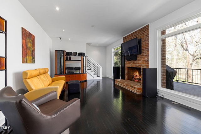 living area featuring dark wood finished floors, recessed lighting, visible vents, stairway, and a brick fireplace